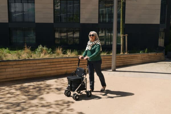 Kvinde går med sin Care One letvægts rollator på 6kg med stort opbevaringsrum under sædet